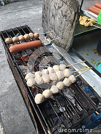 Hand of street vendor`s hand is cooking of meatball pork balls and sausage grill on charcoal stove at street food market Thailand Stock Photo