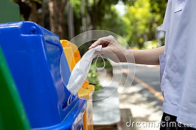 Hand of student girl is throwing away the used protective face mask in the garbage bin,trash bins that separates only a mask and Stock Photo