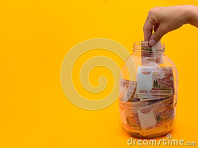 Hand stuffs a five thousandth bill into a glass jar Stock Photo