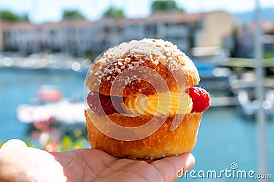 Hand with Tarte tropezienne or La Tarte de Saint-Tropez - dessert pastry consisting of filled brioche with cream and fresh berries Stock Photo