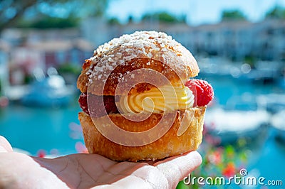 Hand with Tarte tropezienne or La Tarte de Saint-Tropez - dessert pastry consisting of filled brioche with cream and fresh berries Stock Photo