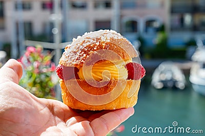 Hand with Tarte tropezienne or La Tarte de Saint-Tropez - dessert pastry consisting of filled brioche with cream and fresh berries Stock Photo