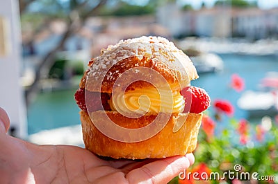 Hand with Tarte tropezienne or La Tarte de Saint-Tropez - dessert pastry consisting of filled brioche with cream and fresh berries Stock Photo