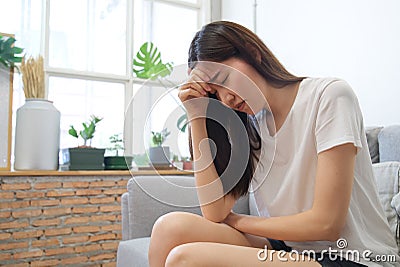 Hand on temples of young unhappy sadness Asian girl sitting on sofa. She is feeling not very good due to her sickness and having a Stock Photo