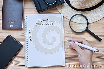 Hand traveler writing Travel Checklist word on notebook with accessories, Camera, Passport, Magnifying, smart Phone and hat on Stock Photo