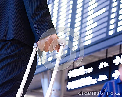 Hand of traveling businessman with baggage in front of airport timetable Stock Photo