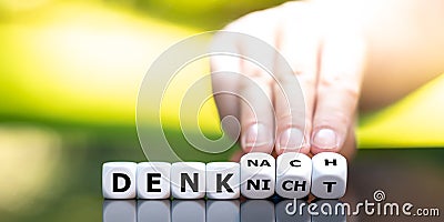 Hand turns dice and changes the German expression `denk nicht` do not think to `denk nach` think. Stock Photo