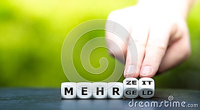 Hand turns dice and changes the German expression `mehr Geld` more money to `mehr Zeit` more time. Stock Photo