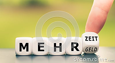 Hand turns dice and changes the German expression `mehr Geld` `more money` to `mehr Zeit` `more time`. Stock Photo