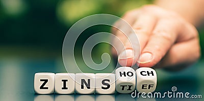 Hand turns dice and changes the German expression `Zinstief` low of interest rates to `Zinshoch` peak of interest rates. Stock Photo