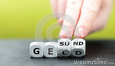 Hand turns dice and changes the German word `Geld` money to `Gesund` health. Stock Photo