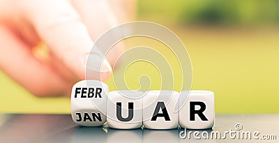 Hand turns a dice and changes the German word `Januar` `January` in English to `Februar` `February` in English. Stock Photo