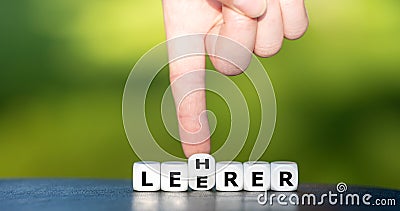 Hand turns dice and changes the German word `Leerer` empty to `Lehrer` teacher. Stock Photo