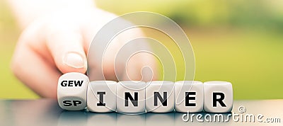 Hand turns dice and changes the German word `Spinner` `weirdo` to `Gewinner` `winner`. Stock Photo