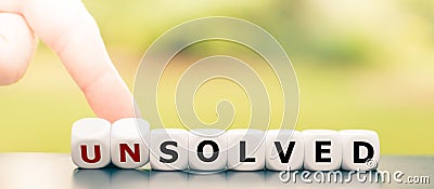 Hand turns dice and changes the word `unsolved` to `solved`. Stock Photo