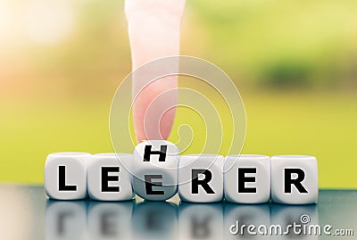 Hand turns a dice and corrects a typo by changing the German word `Leerer` `empty` in English to `Lehrer` `teacher` in Stock Photo