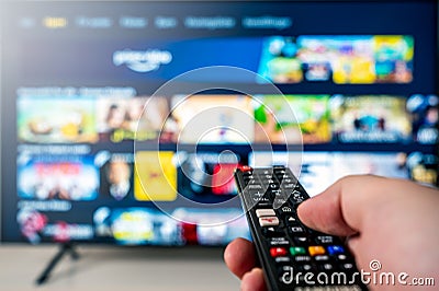 Hand with tv remote aimed towards big 4k flat screen oled tv with blurred out tv entertainment system meny. Stock Photo