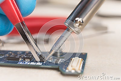 Hand with tweezers holding the chip, soldering iron solder it in place. Computer repair. Macrophotography. Copy space. Stock Photo