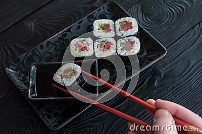Hand using chopsticks pick. Maki-Sushi, tuna-maki rolls on a black stone plate. Fresh made Sushi set with tuna, cheese and cucumbe Stock Photo
