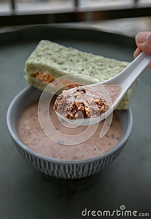 Hand using spoon picking up malt flakes granola in almond milk served with sandwich on ceramic bowl Stock Photo