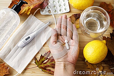 Hand with vitamin D, vitamin C and zinc pills on background of fall leaves, face mask, lemons Stock Photo