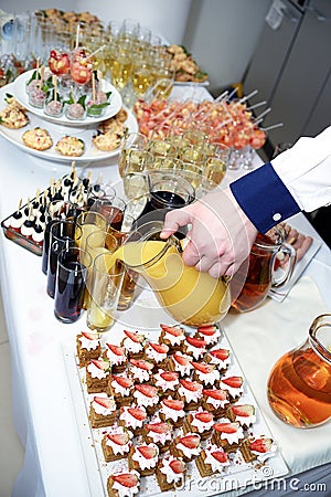 The hand of the waiter pours orange juice from a jug Stock Photo