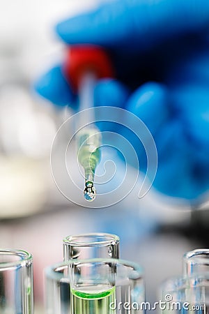 Hand wearing blue gloves holding droper and dropping water drop into test tube Stock Photo