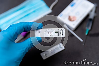 A hand wearing a protective glove is seen holding a rapid Covid test, also known as antigen test or lateral flow test, showing a Stock Photo