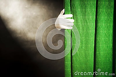 Hand in white glove on a background of green curtains, with the light from the reflector on a black background Stock Photo