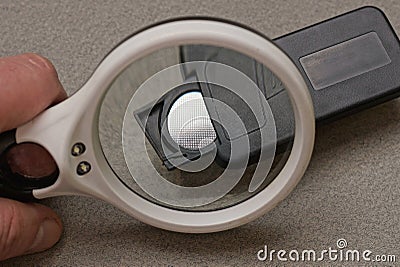 Hand with a white magnifying glass magnifies a black plastic remote control Stock Photo