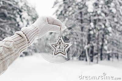 A hand in white mittens and a sweater holds a carved wooden star Stock Photo