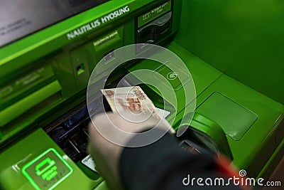 Moscow, Russia, 04/07/2020:Hand withdrawing cash from a brightly colored green ATM. Background in focus. Visible interface Editorial Stock Photo