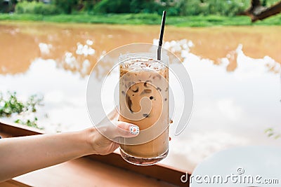 Hand of woman holding glass of iced coffee by riverside Stock Photo