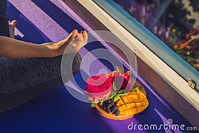 Hand of a woman meditating in a yoga pose, sitting in lotus with fruits in front of her dragon fruit, mango and mulberry Stock Photo