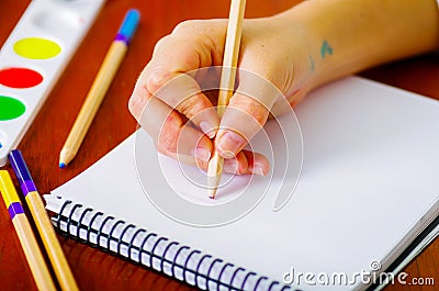 Hand of woman painter writing with color pencils into notebook, paint colors sitting beside on desk Stock Photo