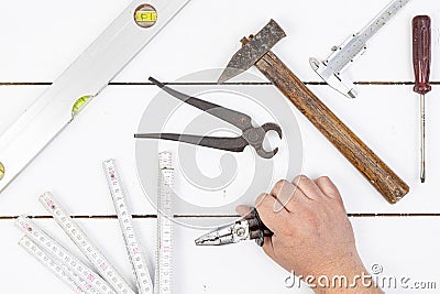 Hand on the wooden board with old used hand tools. Old used hammer, pliers, libella, measuring meter, nonius and screwdriver Stock Photo