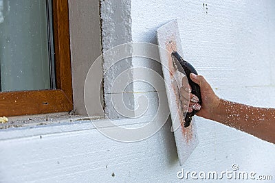 Hand of a worker with a tool for sanding and making smooth and even the surface of a house wall insulated with styrofoam Stock Photo