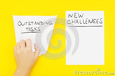 Hand wrinkles piece of paper with phrase: outstanding tasks, and nearby blank sheet of paper with phrase: New challenges Stock Photo