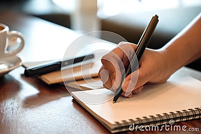 A hand writing down on a white blank notebook with coffee cup on wooden table Stock Photo