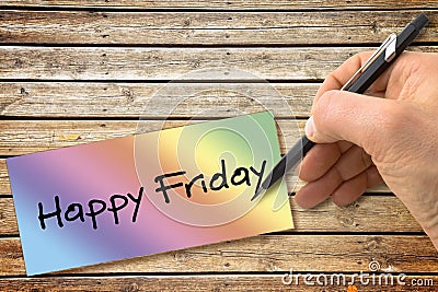 Hand writing Happy Friday with a pencil on a colored sheet over a wooden table Stock Photo