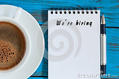 Hand writing We're Hiring on white paper with cup of vorning coffee, View from above Stock Photo