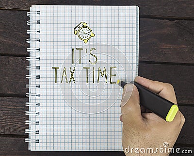 Hand writing It`s tax time on notepad on the dark wooden desk. Stock Photo