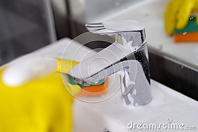 Hand in yellow rubber gloves holding sponge for washing dirty faucet with limescale Stock Photo