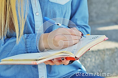 The hand of a young girl dressed in a denim shirt, who writes in a notebook on the street Stock Photo