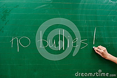 Hand of a young girl writing the words NO BULLIES on the green school board Stock Photo