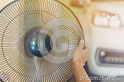 Hand of Young man touch and adjust on front grills of electric fan for a good wind in his home in summer Stock Photo