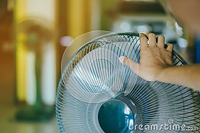 Hand of Young man touch and adjust on front grills of electric fan for a good wind in his home in summer of april Stock Photo