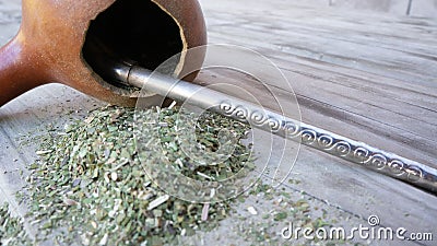 Handcrafted mate made of calabash and a metal straw on a wooden table with weed mate scattered on it Stock Photo