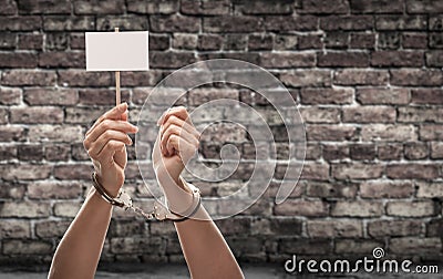 Handcuffed Female Hand Holding Blank Sign Against Aged Brick Wall Stock Photo