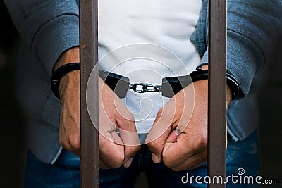 Handcuffed hands of a businessman behind the bars of a prison. C Stock Photo